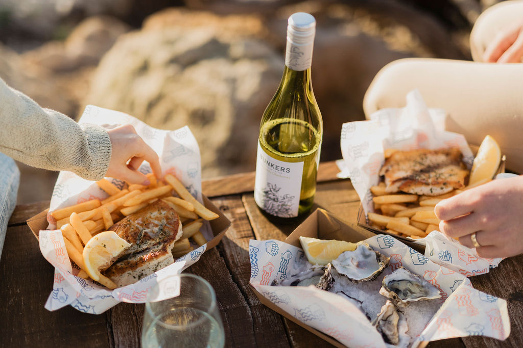 A couple enjoying a bottle of Bunkers wine with oysters and fish and chips 